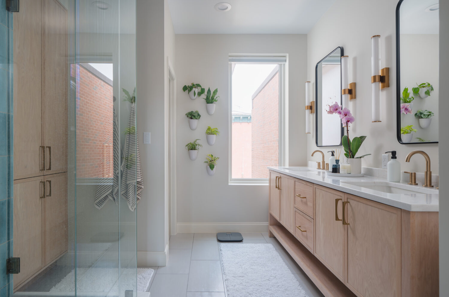 Luxury primary bathroom renovation in DC home with custom light wood double vanity, white countertops, brass fixtures, and designer sconce lighting by Hammer Design Build Remodel