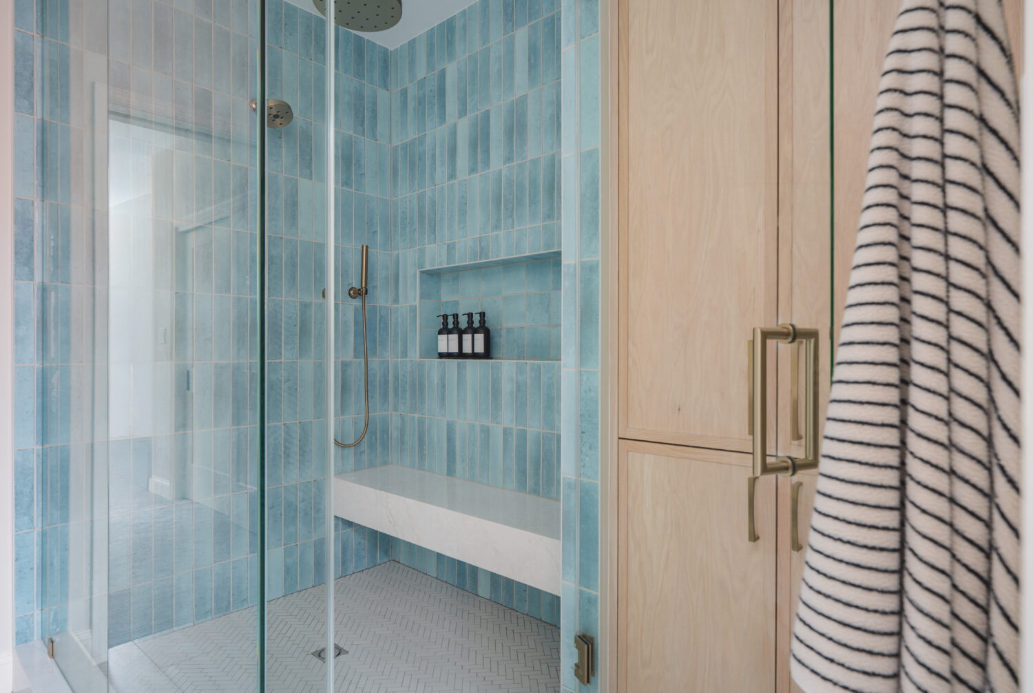 Spa-like primary bathroom remodel in Washington DC featuring custom wood vanity, aqua blue vertical tile shower with bench, and frameless glass enclosure