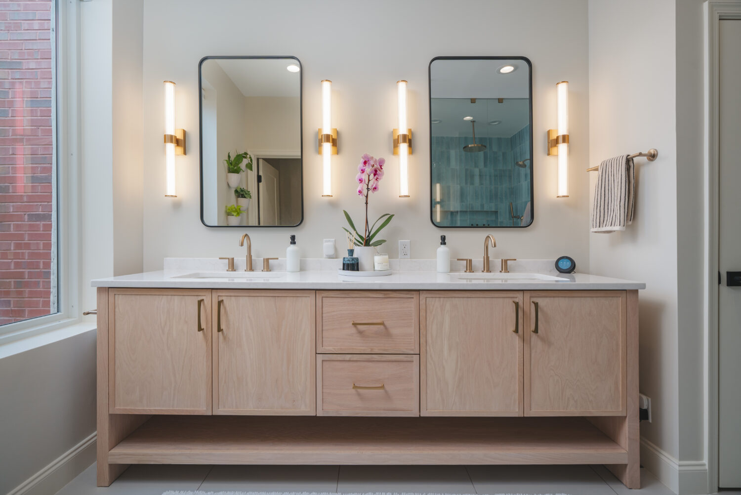 Luxury primary bathroom renovation in DC home with custom light wood double vanity, white countertops, brass fixtures, and designer sconce lighting by Hammer Design Build Remodel