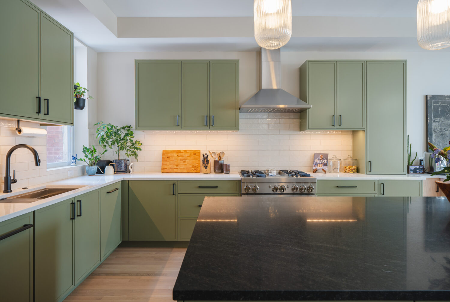 Modern Washington DC kitchen renovation featuring custom sage green cabinetry, natural white oak floors, black countertop island with seating, and pendant lighting by Hammer Design Build Remodel