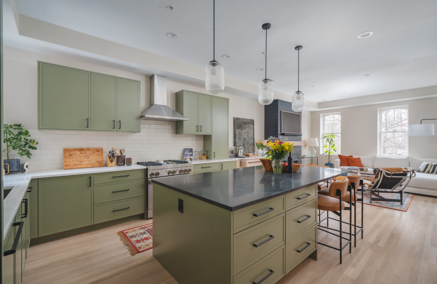 Modern Washington DC kitchen renovation featuring custom sage green cabinetry, natural white oak floors, black countertop island with seating, and pendant lighting by Hammer Design Build Remodel