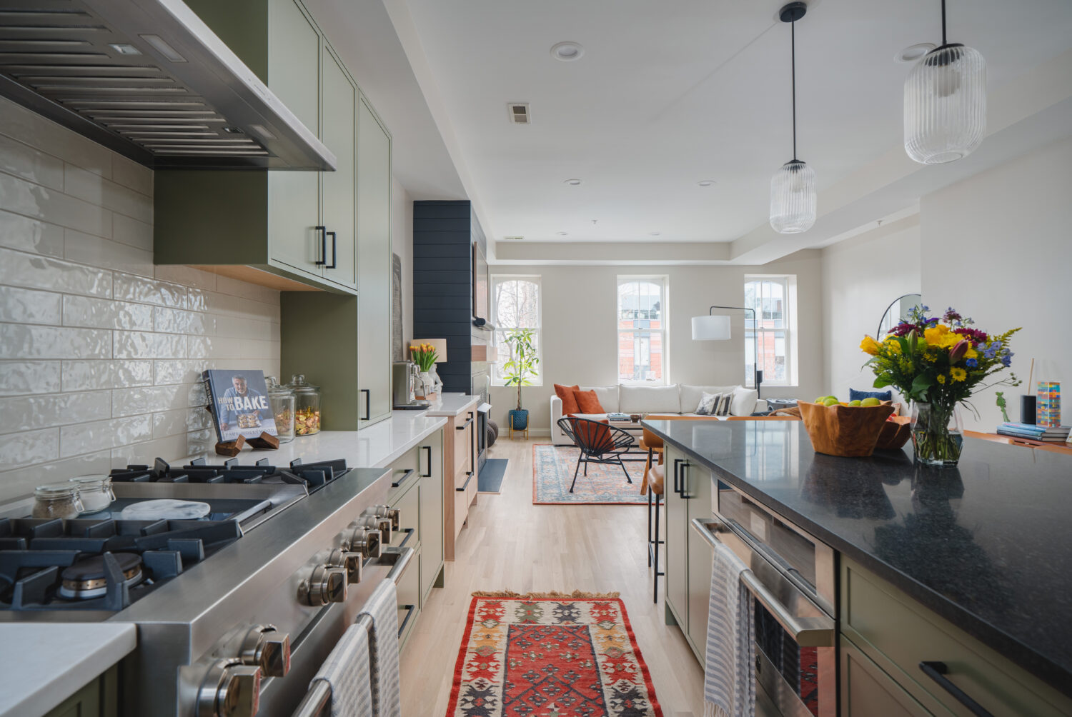 Modern Washington DC kitchen renovation open to the dining room, featuring custom sage green cabinetry, natural white oak floors, black countertop island with seating, and pendant lighting by Hammer Design Build Remodel